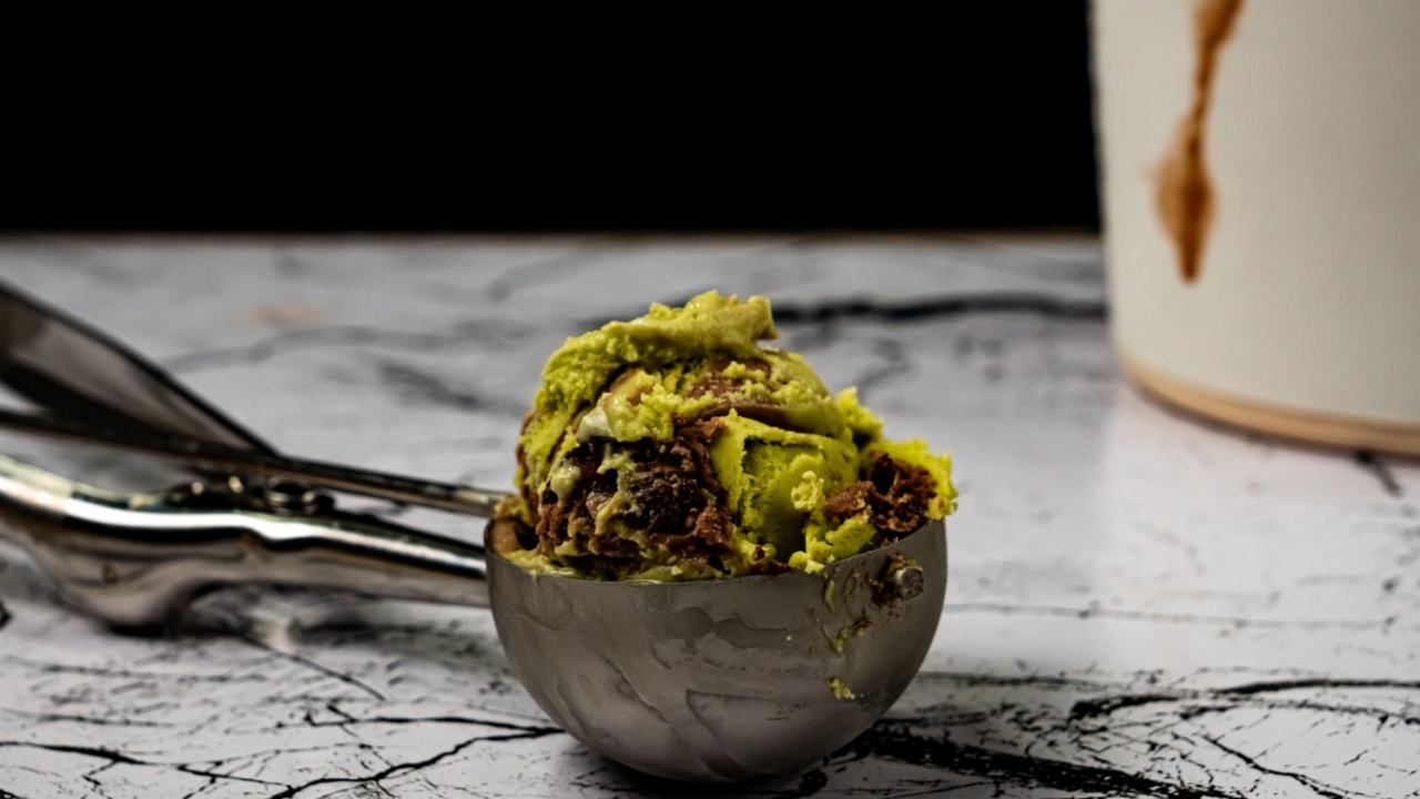 Delicious scoop of pistachio and chocolate ice cream served in a stainless steel scooper on a marble table background