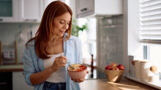 Smiling woman eating oatmeal with fresh fruit in the morning.
