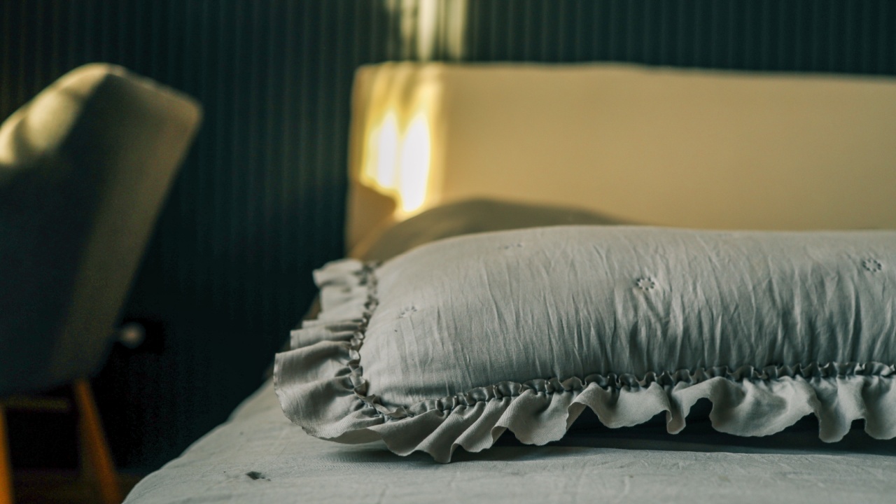 Close-up of a soft pillow with delicate ruffles on a neatly made bed, bathed in gentle morning light, creating a calm and cozy bedroom atmosphere.