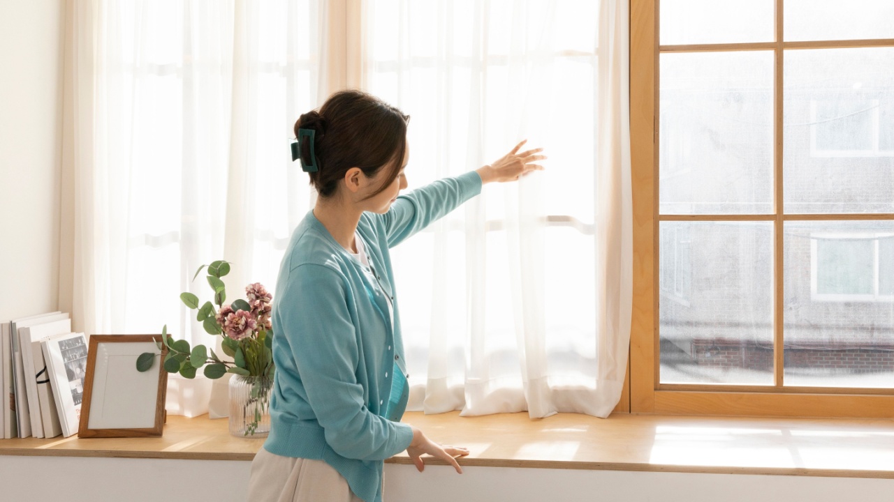 Woman opening sheer curtains to let in morning light in a cozy modern room