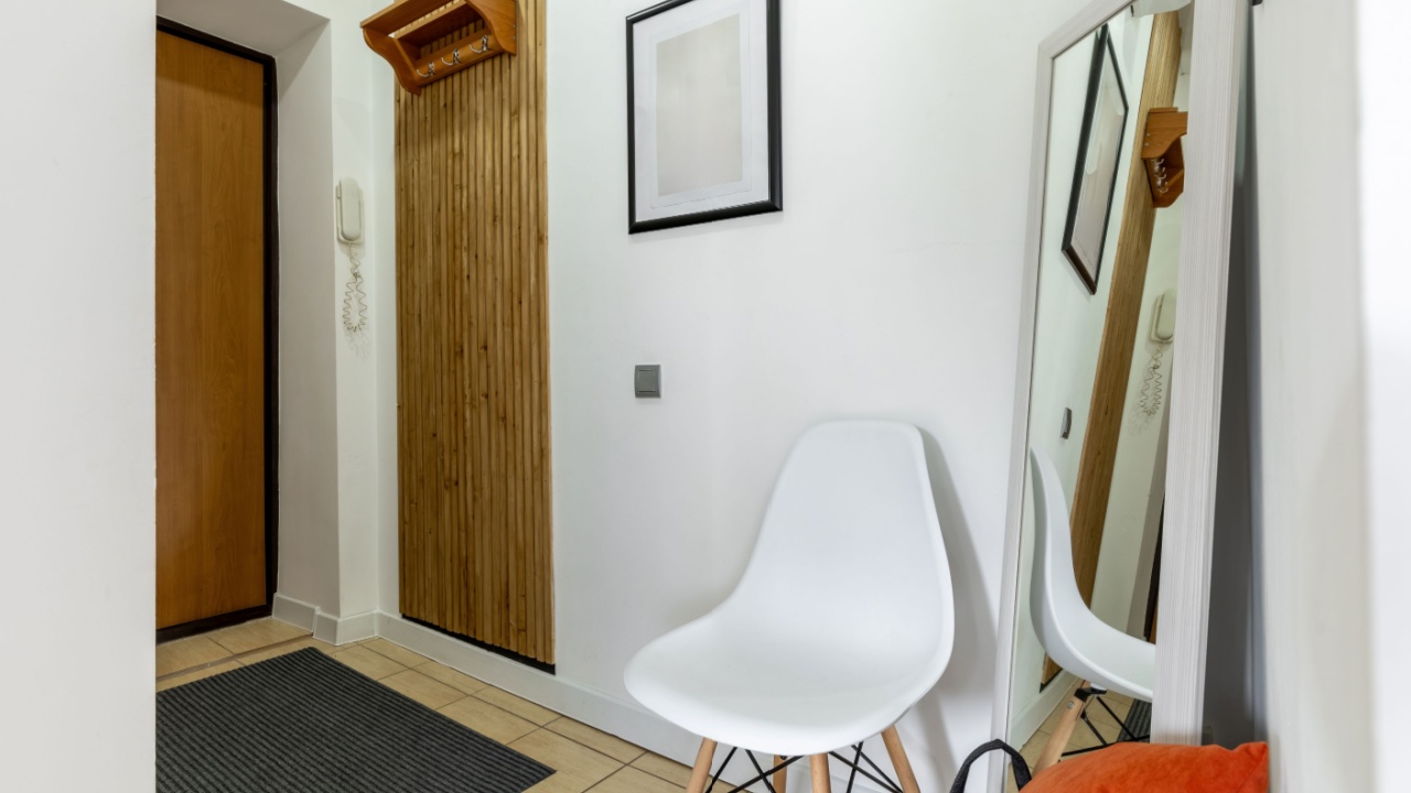 Modern entryway featuring a wooden wall panel, white chair, leaning mirror, framed artwork, and a telephone near the door.
