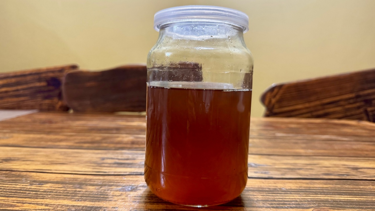 A glass jar filled with rendered pork lard placed on a rustic wooden table. Traditional homemade fat used in cooking and food preservation.