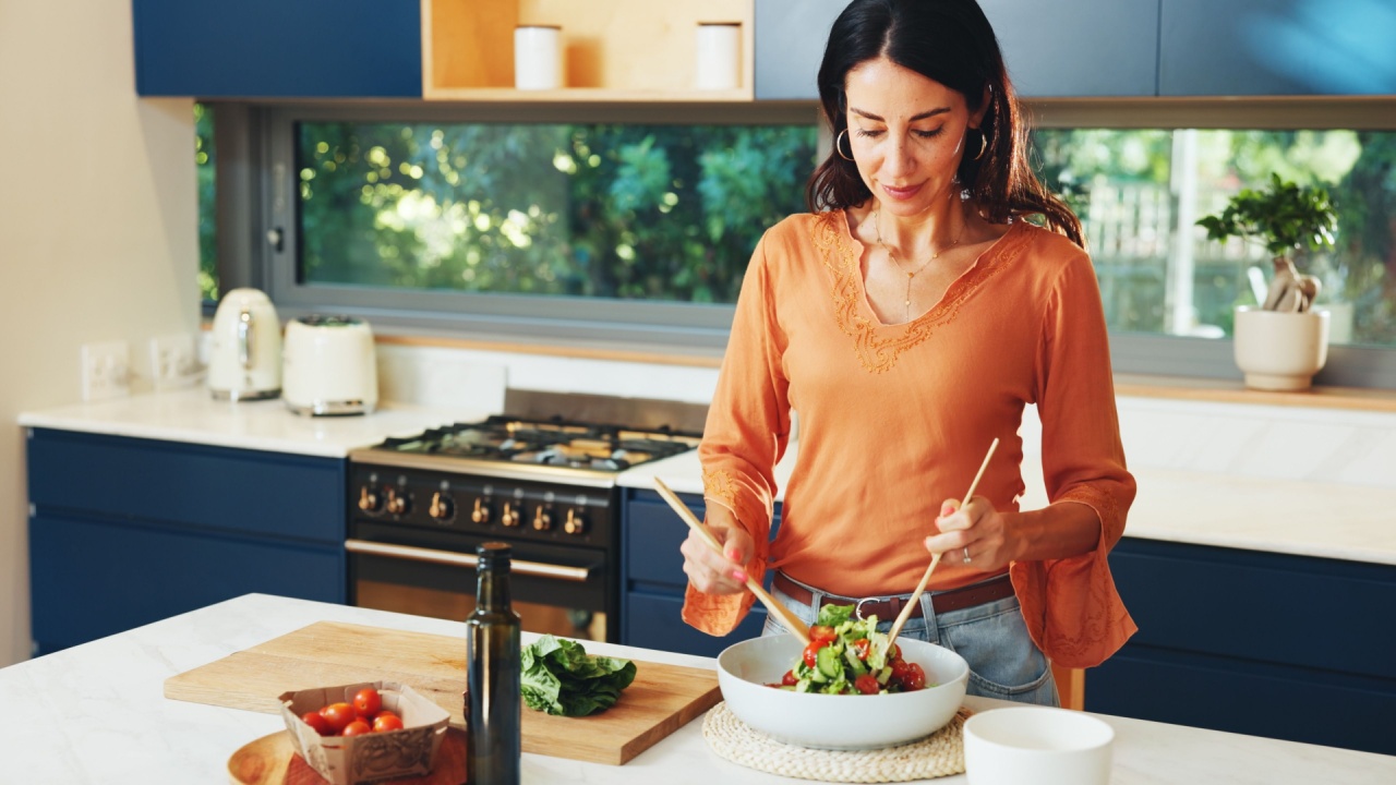 Cooking, salad and woman mix vegetable for healthy diet, nutrition or ingredients in home kitchen. Vegan, meal prep or person make lunch with leafy greens, natural tomato or organic food for wellness