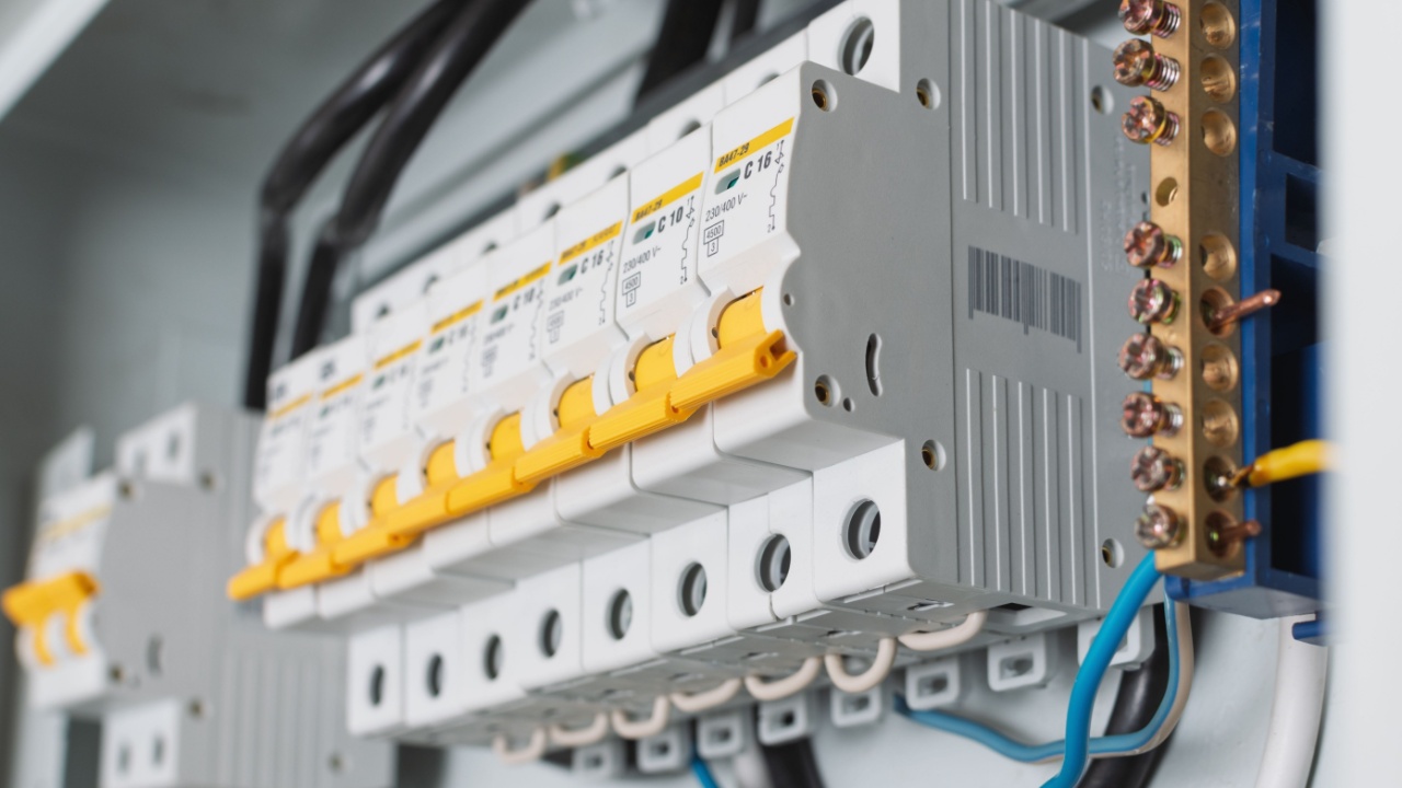 Close-up view of circuit breakers with yellow levers in a distribution panel highlights precision wiring, copper busbar, and technical details of home electrical installation.