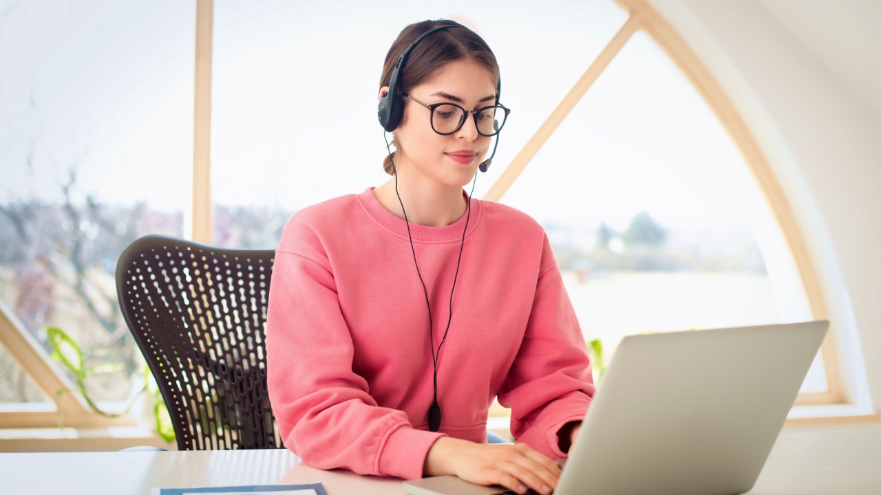 Customer service assistant wearing headset while sitting behind her computer and working in the call center. 