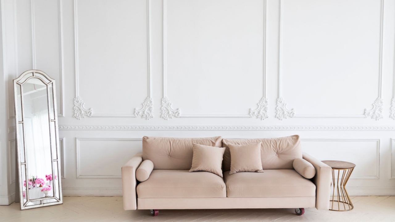 Elegant classic interior with sofa, full-length mirror, metal coffee table against white wall with decorative molding — luxurious living room design with minimal color palette and timeless aesthetics