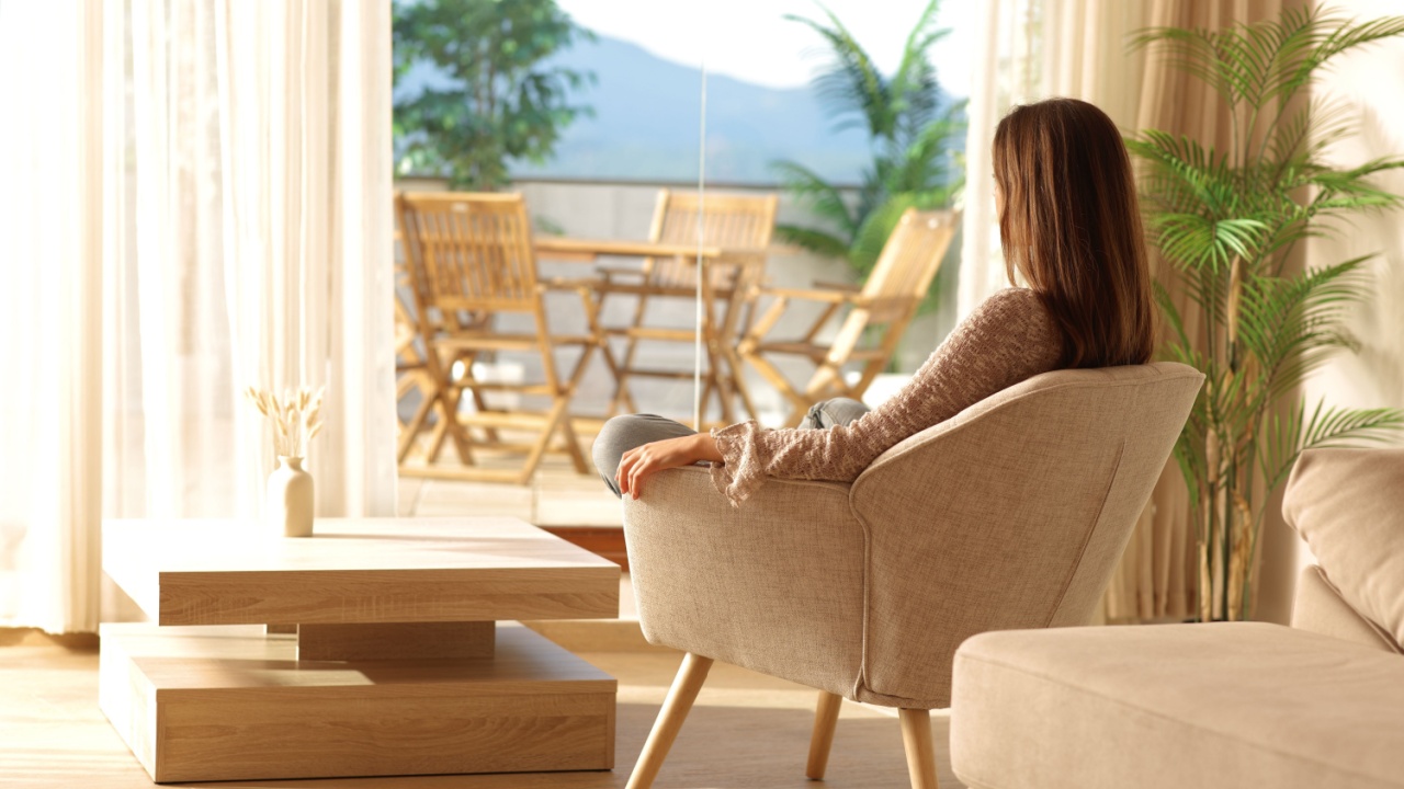 Woman sitting on armchair looking through a window relaxing at home