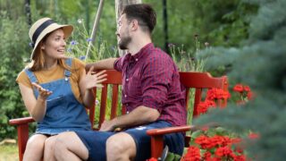 Female and male gardeners sitting on a bench surrounded by flowers and having an engaging conversation. Resting after working hard