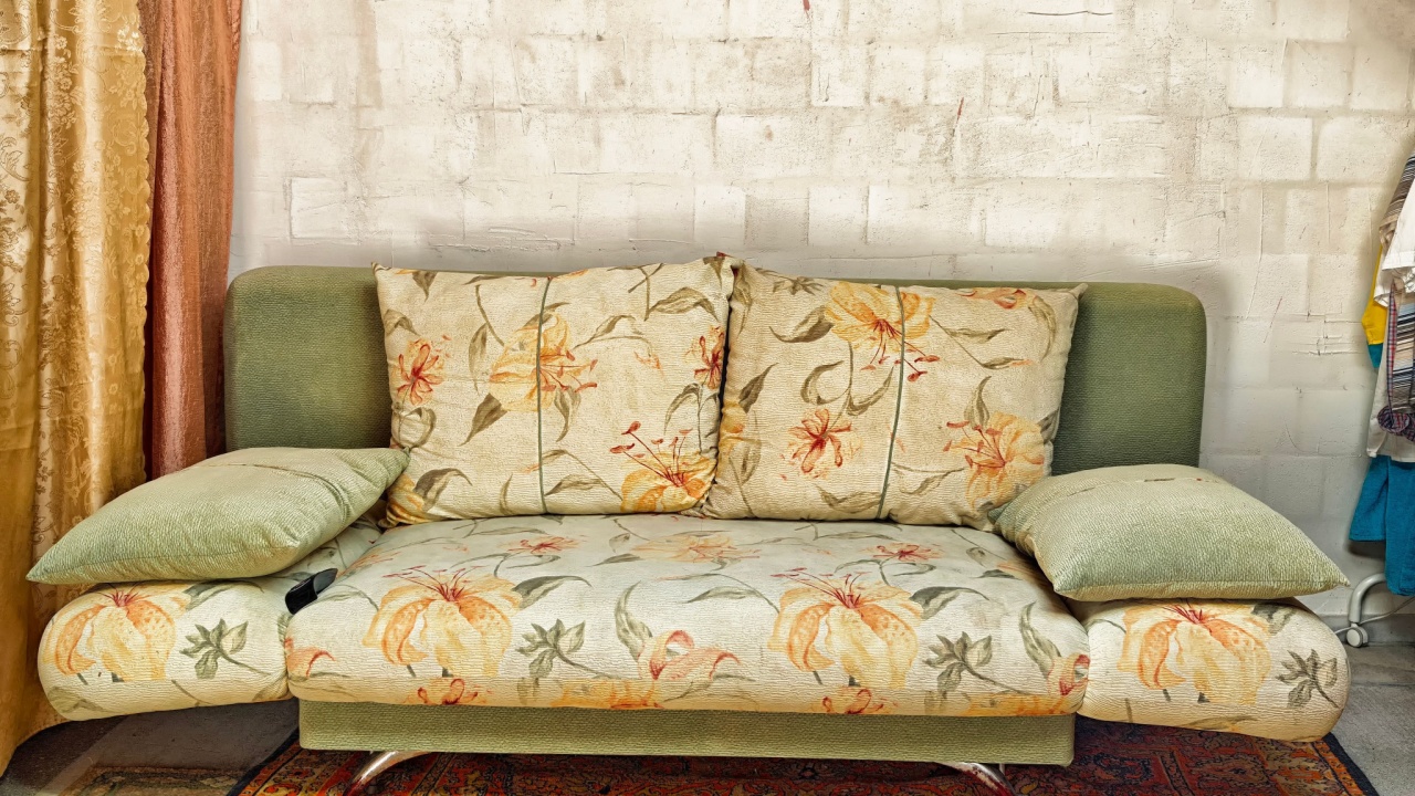 A floral patterned couch with soft green and beige tones is positioned against a textured wall, surrounded by warm curtains and an intricate rug.