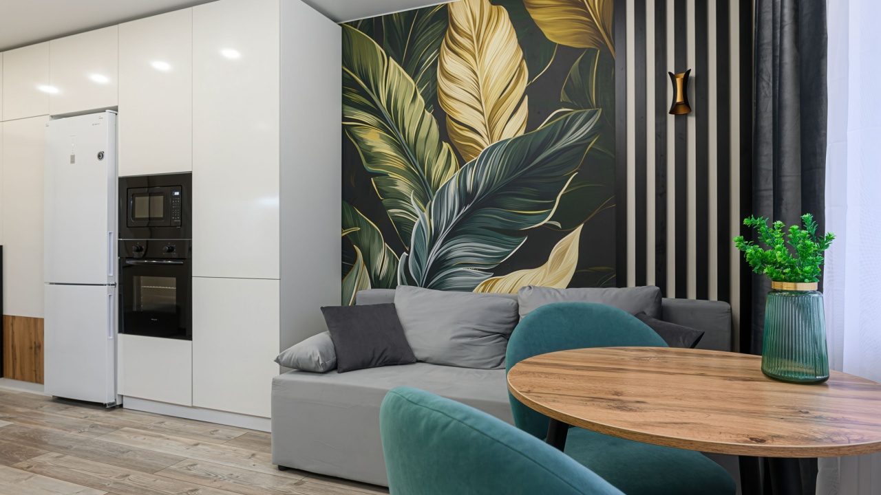 modern living space with a kitchen corner, featuring a grey sofa, round wooden table, turquoise chairs, and a botanical wall mural