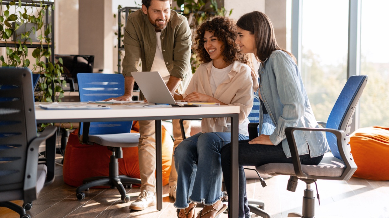 Three marketing managers are collaborating on a project, using a laptop in a modern office space with natural light and comfortable seating. Teamwork concept