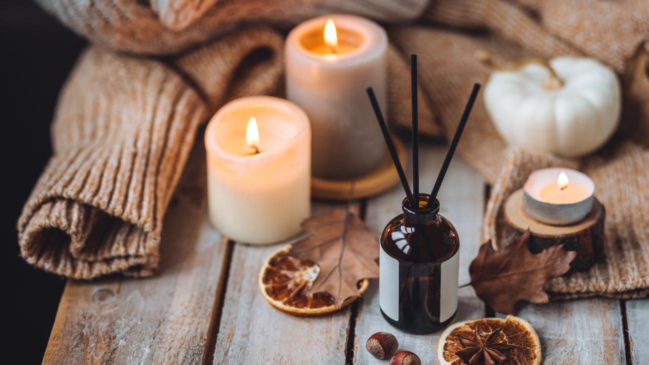 Concept of house decor, apartment seasonal fragrance. Thanksgiving. Autumn mood, cozy fall home atmosphere. Aroma diffuser, pumpkins, knitted warm sweaters, burning candles, dry leaves on wooden table