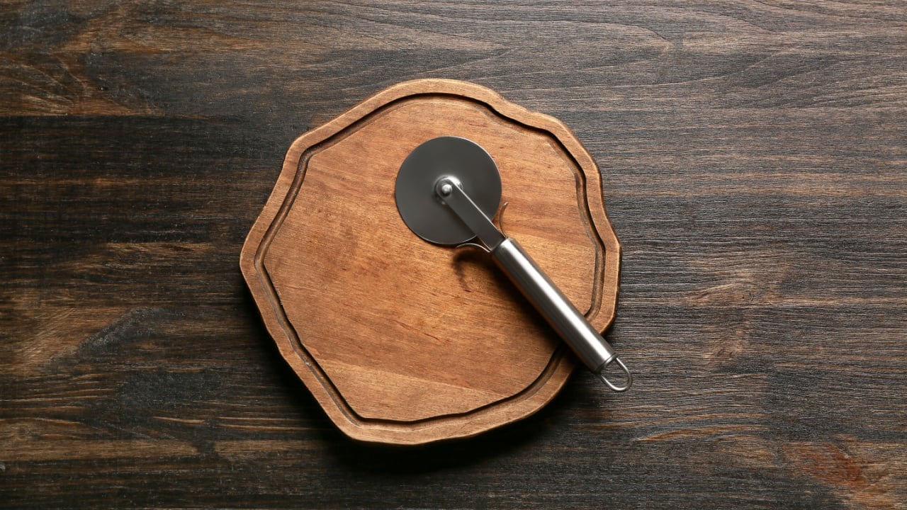 Cutting board with stainless steel pizza cutter on wooden background