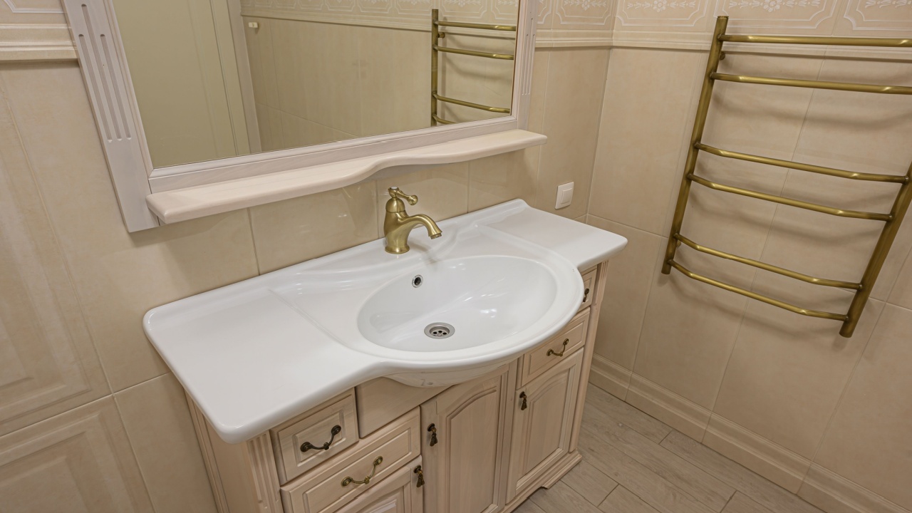 A bathroom scene showcasing a vanity with a white sink, brass faucet, mirror, and a heated towel rack against tiled walls