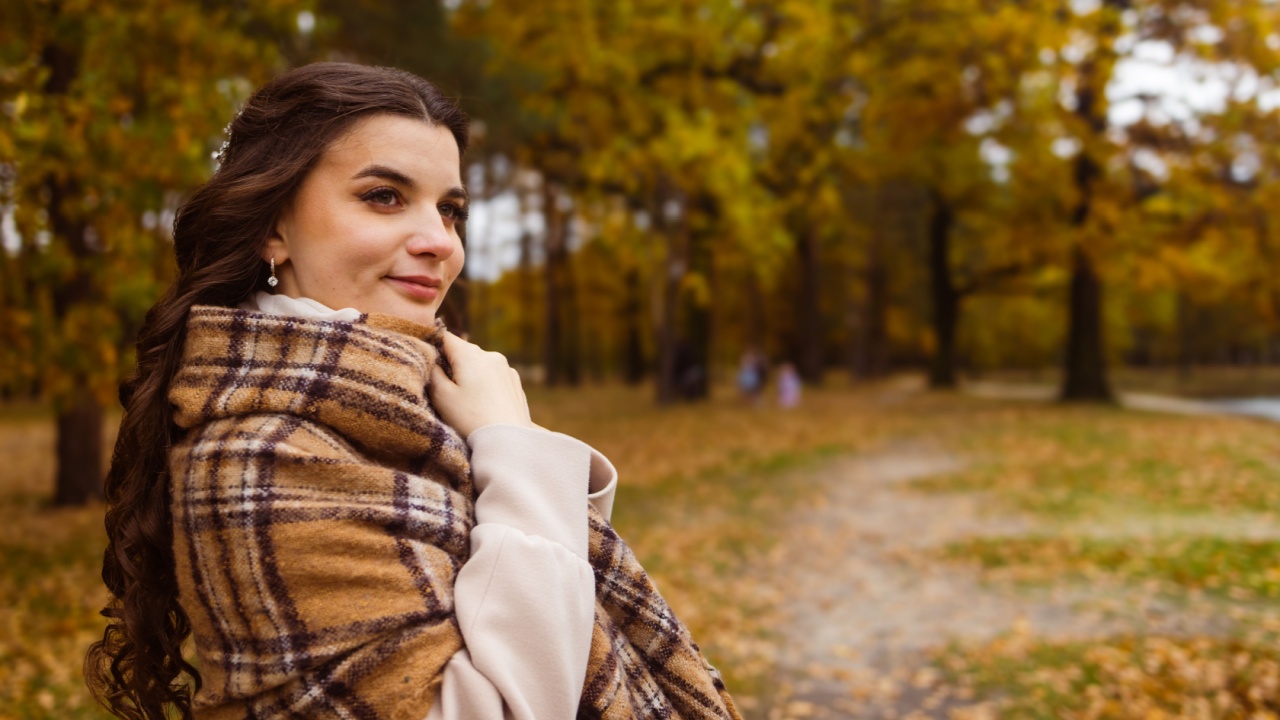 Woman walking in the autumnal park and wearing classy beige coat and scarf, autumnal fashion
