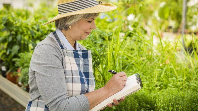 Mature woman in a greenhouse taking notes on a notebook