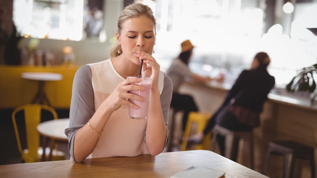 Young beautiful woman drinking milkshake while sitting at table in coffee shop