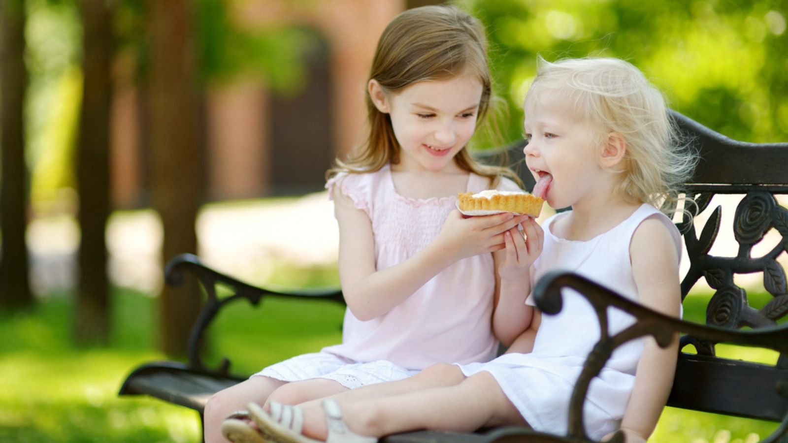 Sisters with cream tart, Two adorable little sisters sharing delicious cream tart outdoors