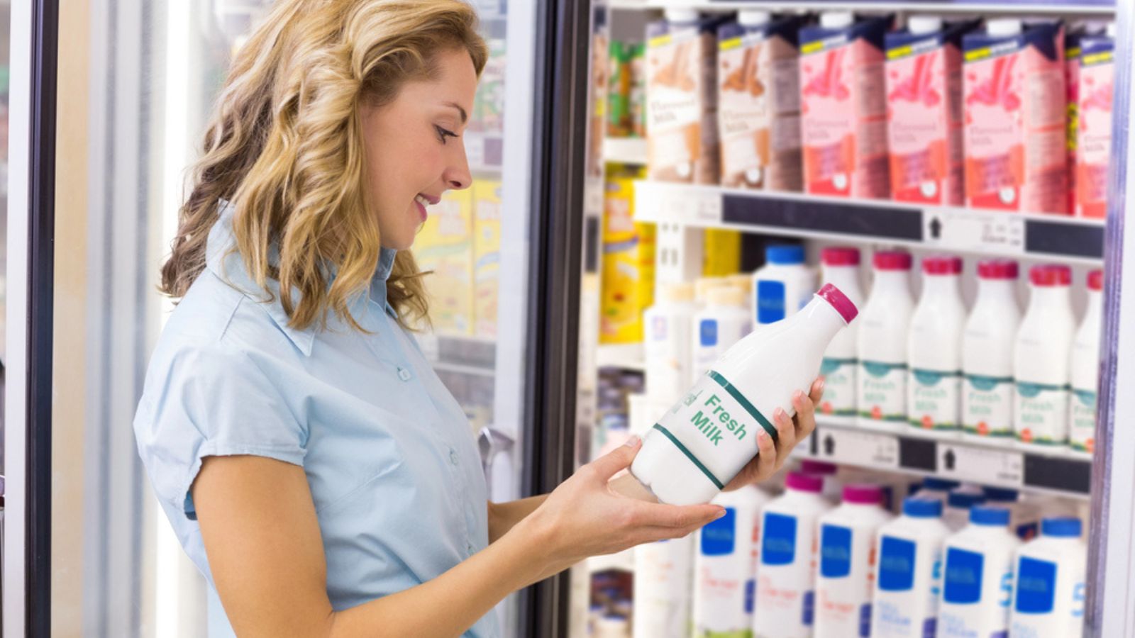 Smiling woman looking at a milk bottle at the grocery
