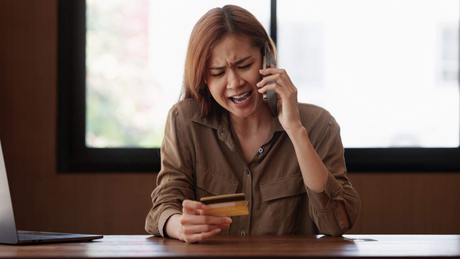 Stressed woman with credit card using laptop at table indoors