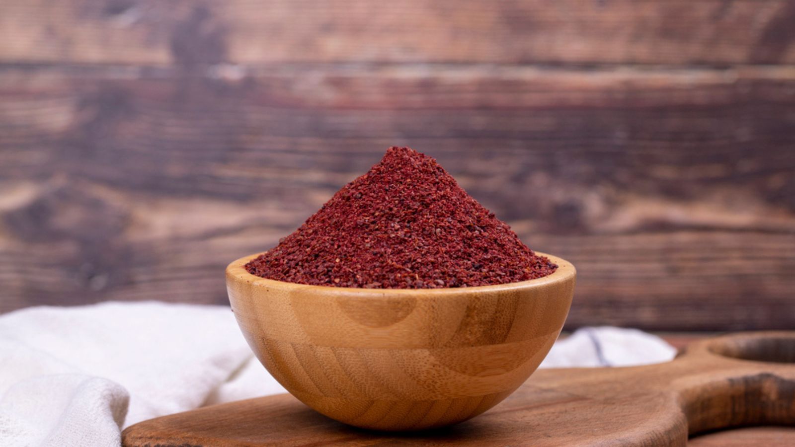 Sumac on wooden background. Dried ground red Sumac powder spices in wooden bowl