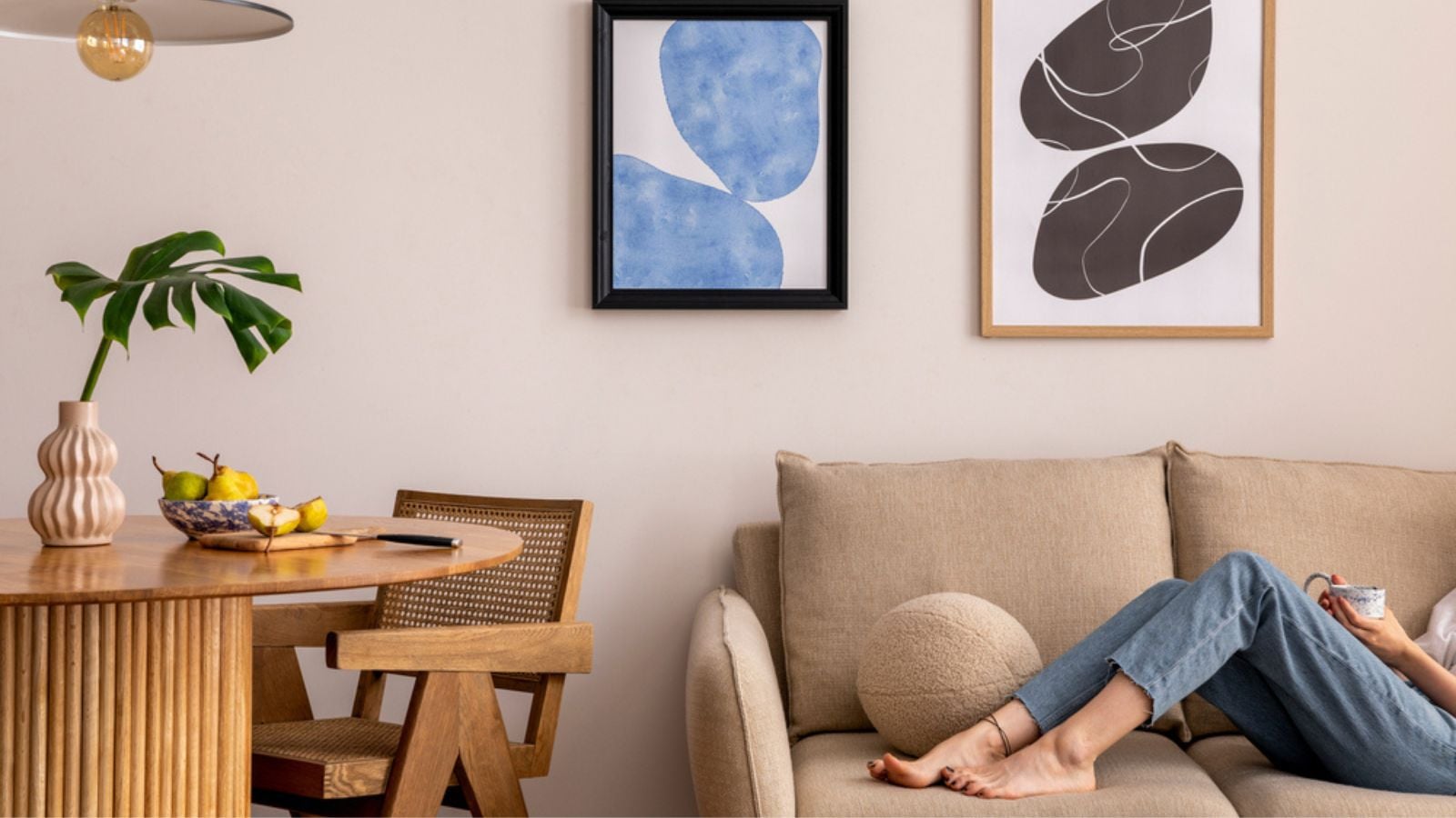 Warm and cozy interior of living room space with two mock up poster frames, round table, leaf in vase, chair, pedant lamp, decoration and woman lying on the sofa. .