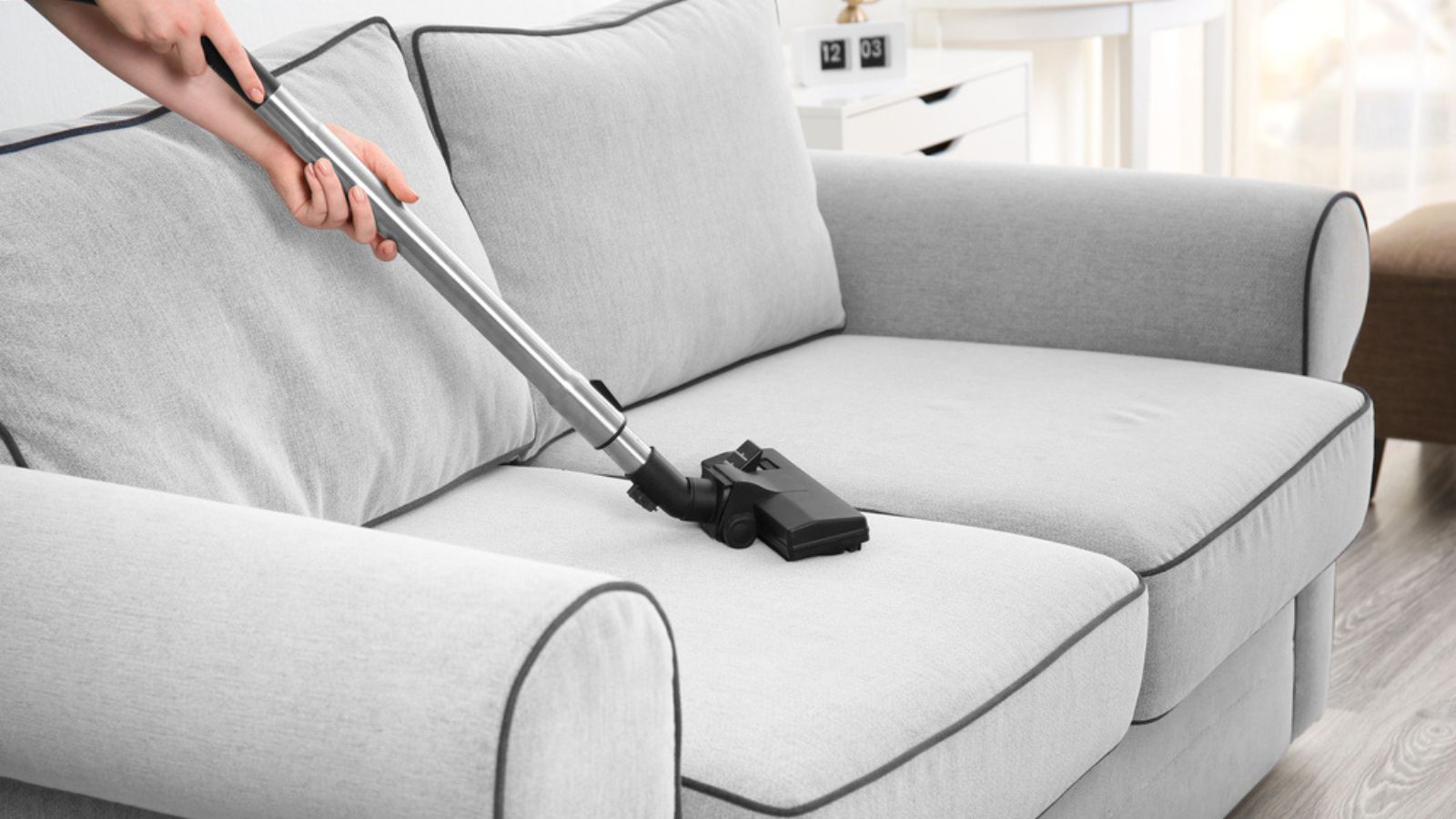 Woman cleaning couch dust with vacuum cleaner at home