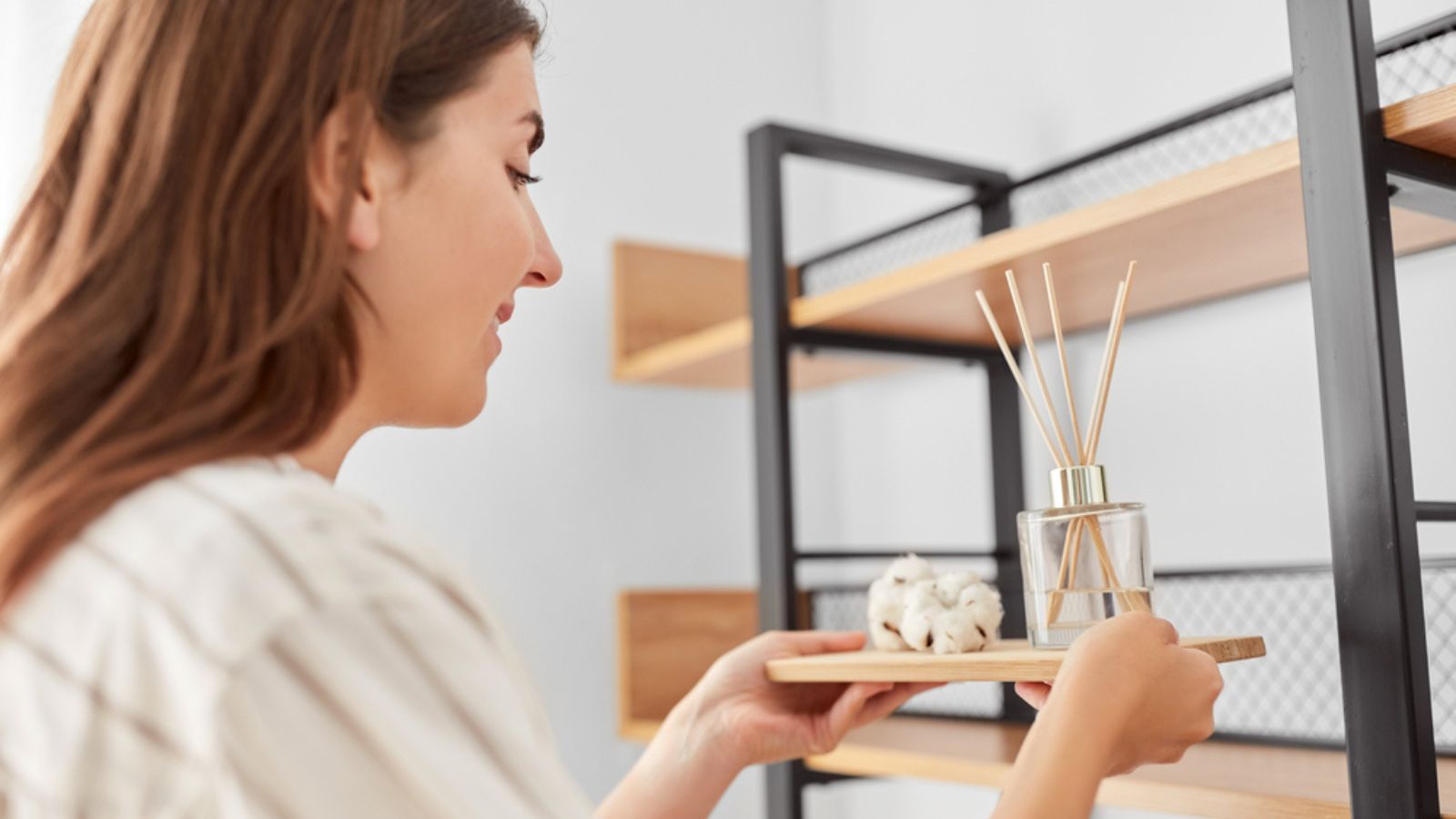 Woman placing aroma reed diffuser to shelf home
