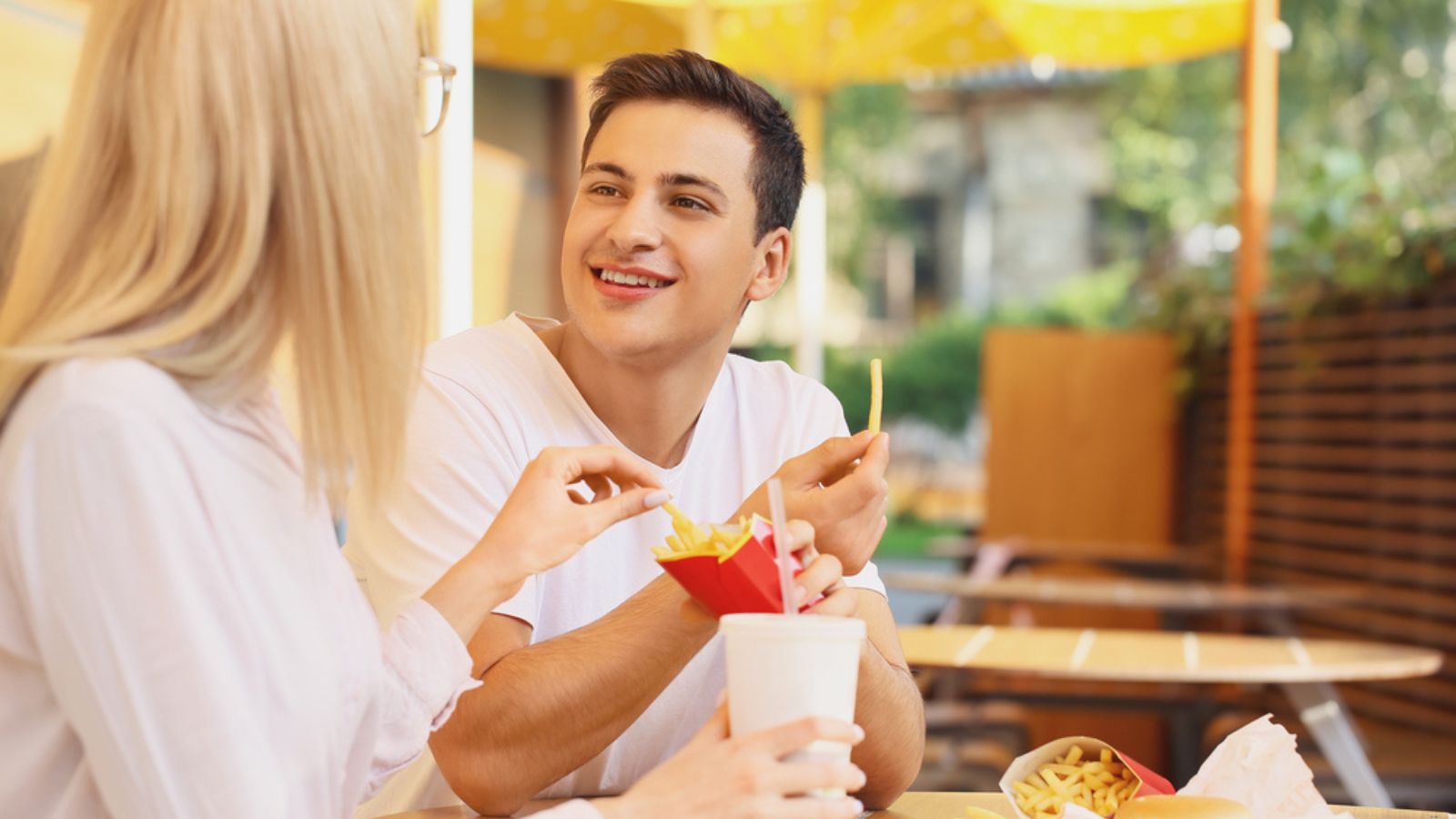 Young couple eating french fries in cafe outdoors