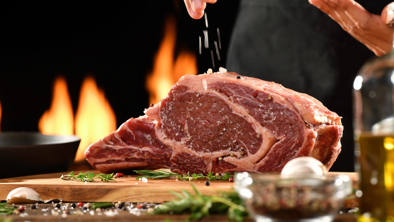 A large raw beef roast being sprinkled with salt