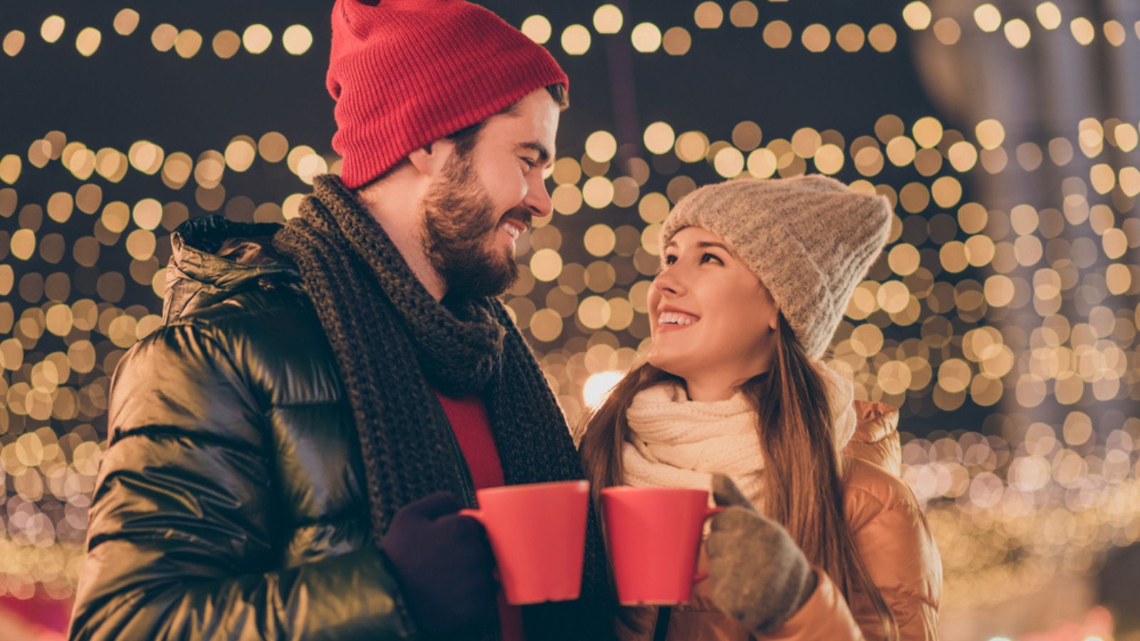 2021 x-mas christmas coming. Boyfriend girlfriend toast cheers eggnog beverage mug under evening outdoors lights wear season coat scarf hat