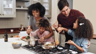 A mother, father, and two children, cook together around a stove