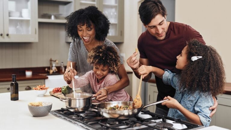 A mother, father, and two children, cook together around a stove