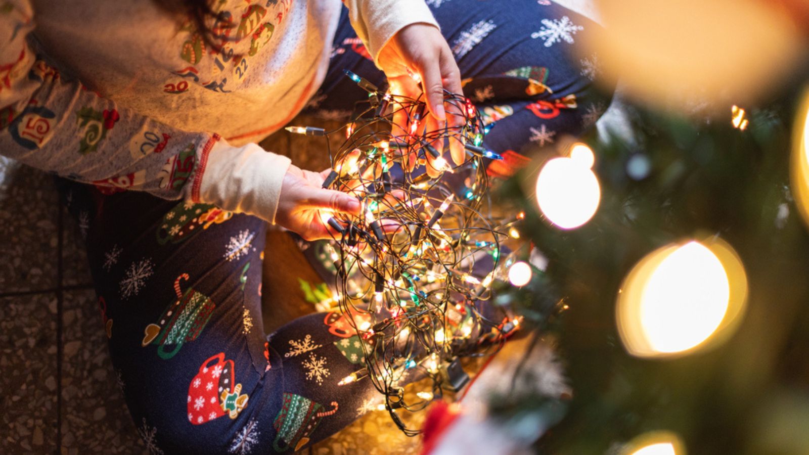 A closeup shot of a person in Christmas pajamas holding illuminated tree lights