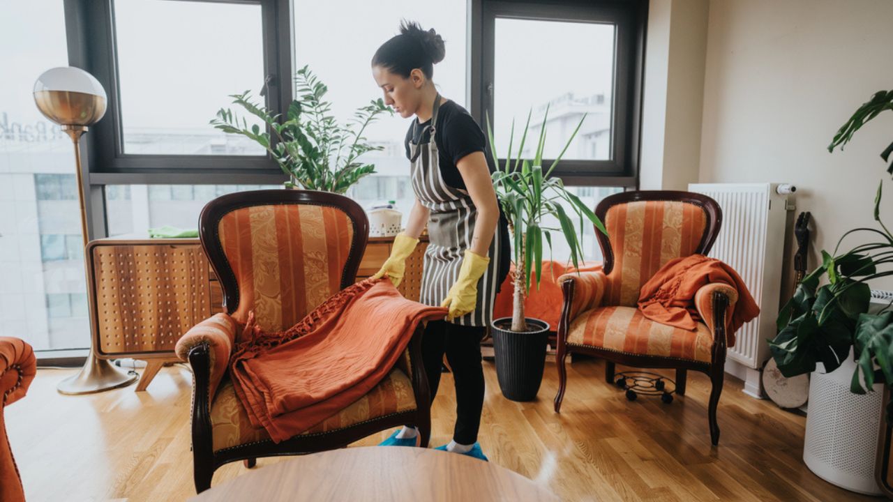 A woman organizes a cozy living room setup, tidying up armchairs and maintaining order.