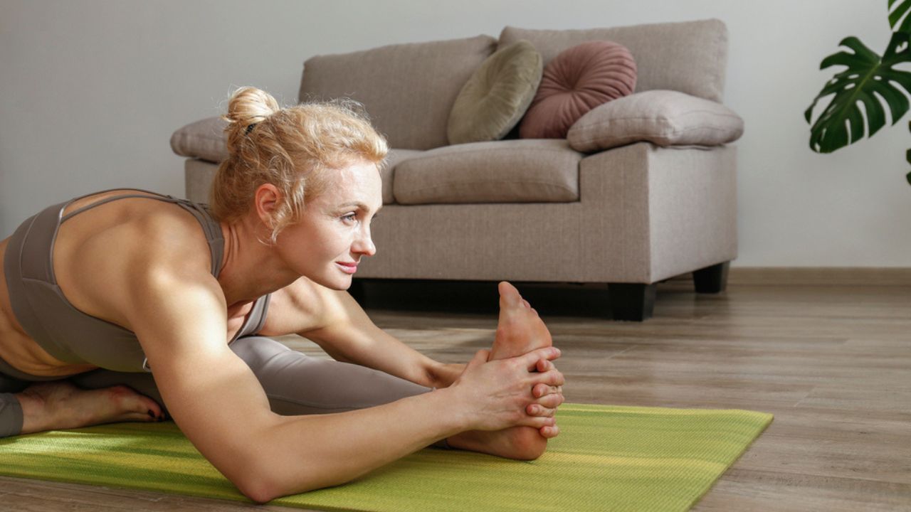 Adult woman doing a one legged seated forward bend on a green mat.