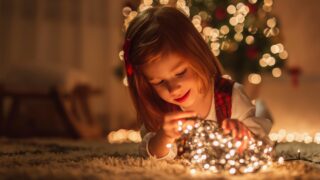 a little girl looks at Christmas lights in front of a Christmas tree.