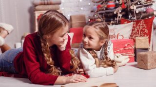 two girls read together in front of a Christmas tree