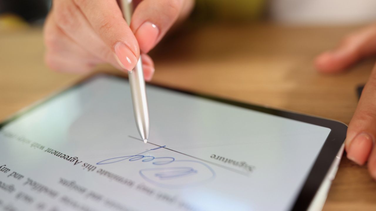 Close-up of female hand signing e-document on tablet with stylus. Electronic signature and modern technologies concept