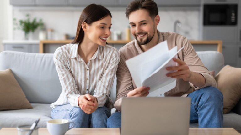 Content young spouses with papers and laptop computer, engaged in discussion and financial planning in cozy living room