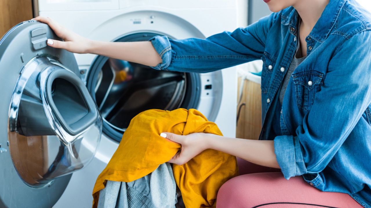 Cropped shot of smiling young woman taking laundry from washing machine