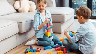 Cute siblings playing with building blocks while sitting on floor in living room