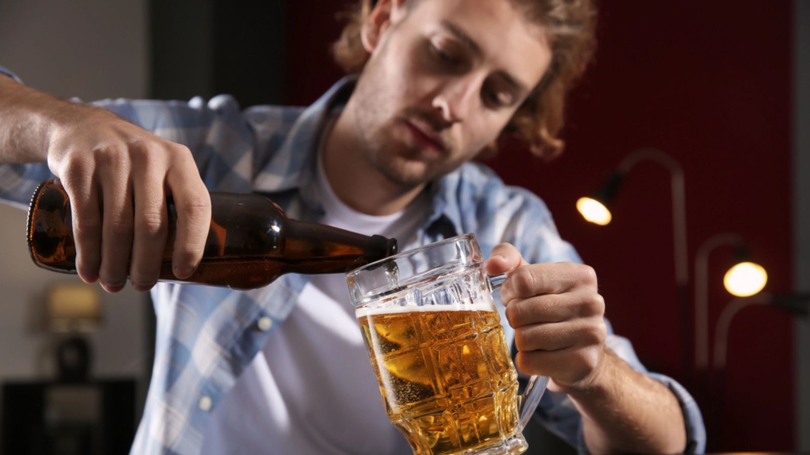 Depressed young man drinking beer at table