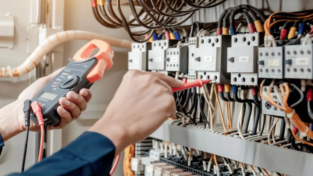Electrician engineer uses a multimeter to test the electrical installation and power line current in an electrical system control cabinet