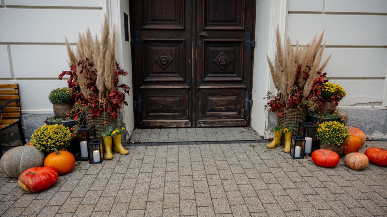 Front door decorated for autumn with pumpkins, gourds, colorful flowers, pampas grass, lanterns, yellow rain boots and rustic fall arrangements creating a cozy welcome