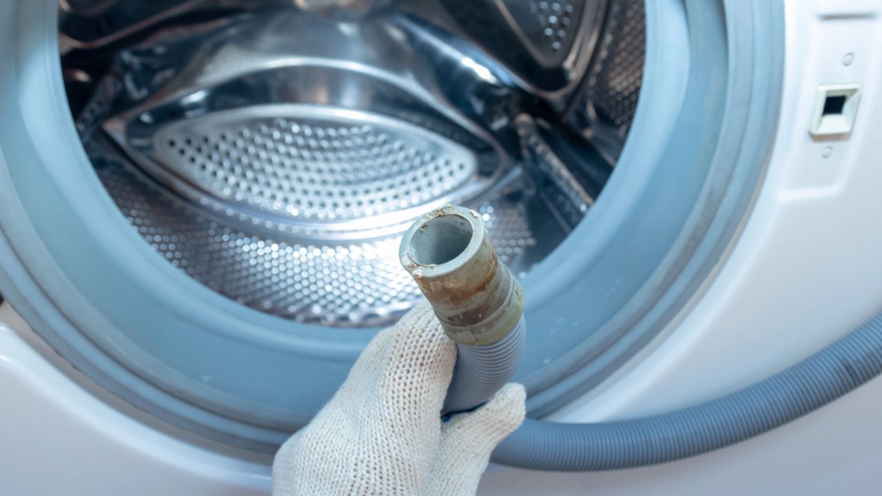 Hand of a plumber holding a broken flexible drain hose of washing machine
