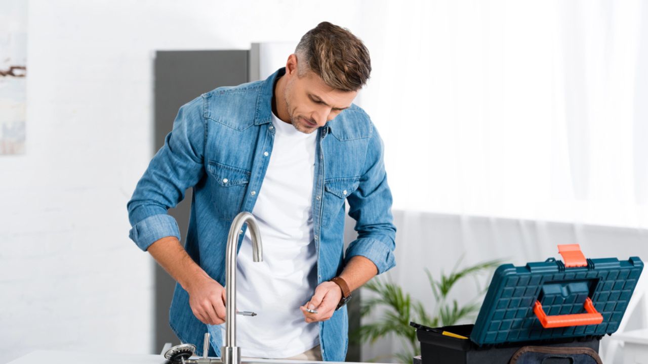 Handsome adult man repairing faucet at kitchen