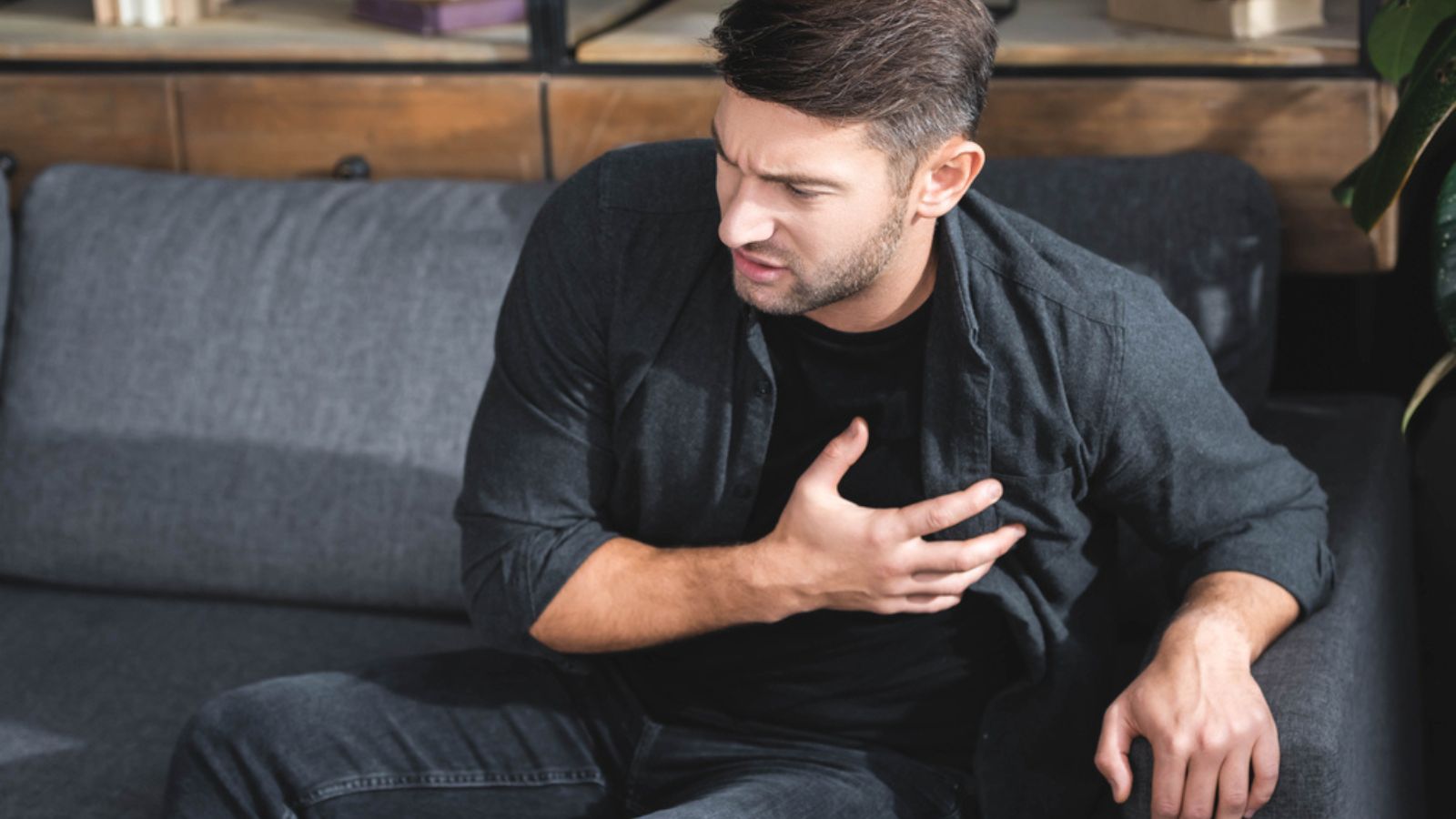 Handsome man in shirt having heart attack in apartment