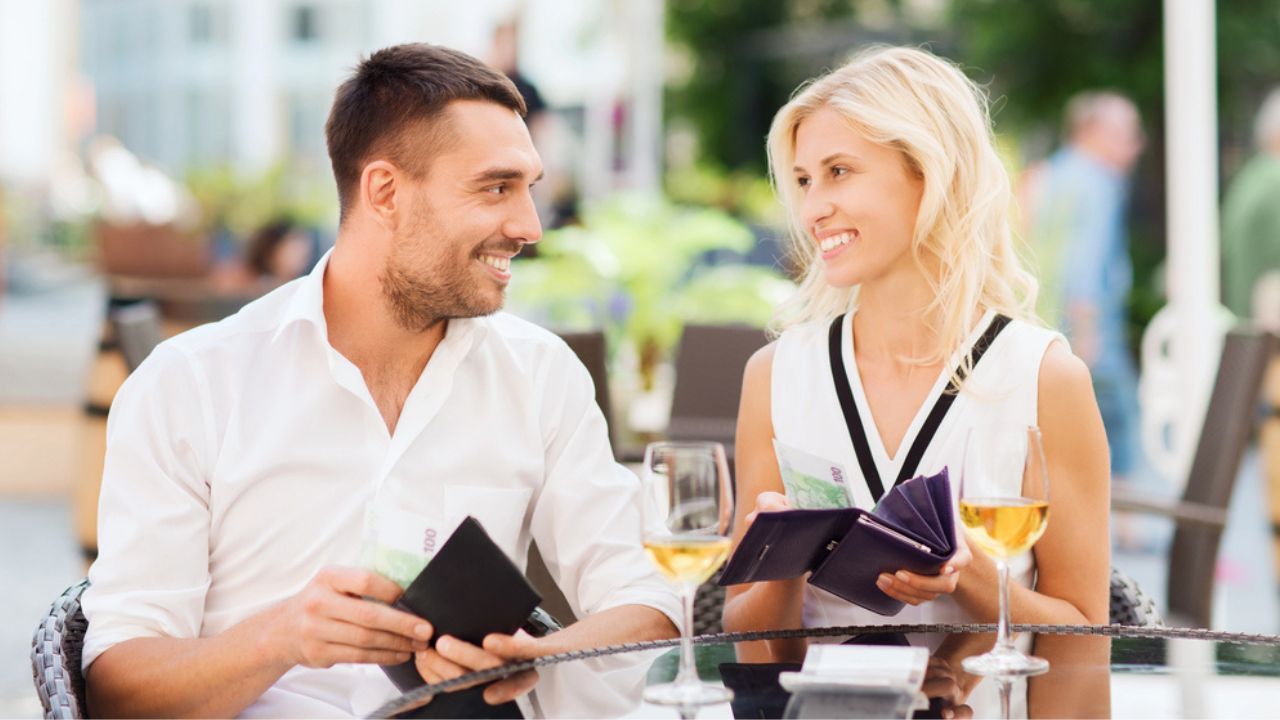 Happy couple with wallet paying bill at restaurant