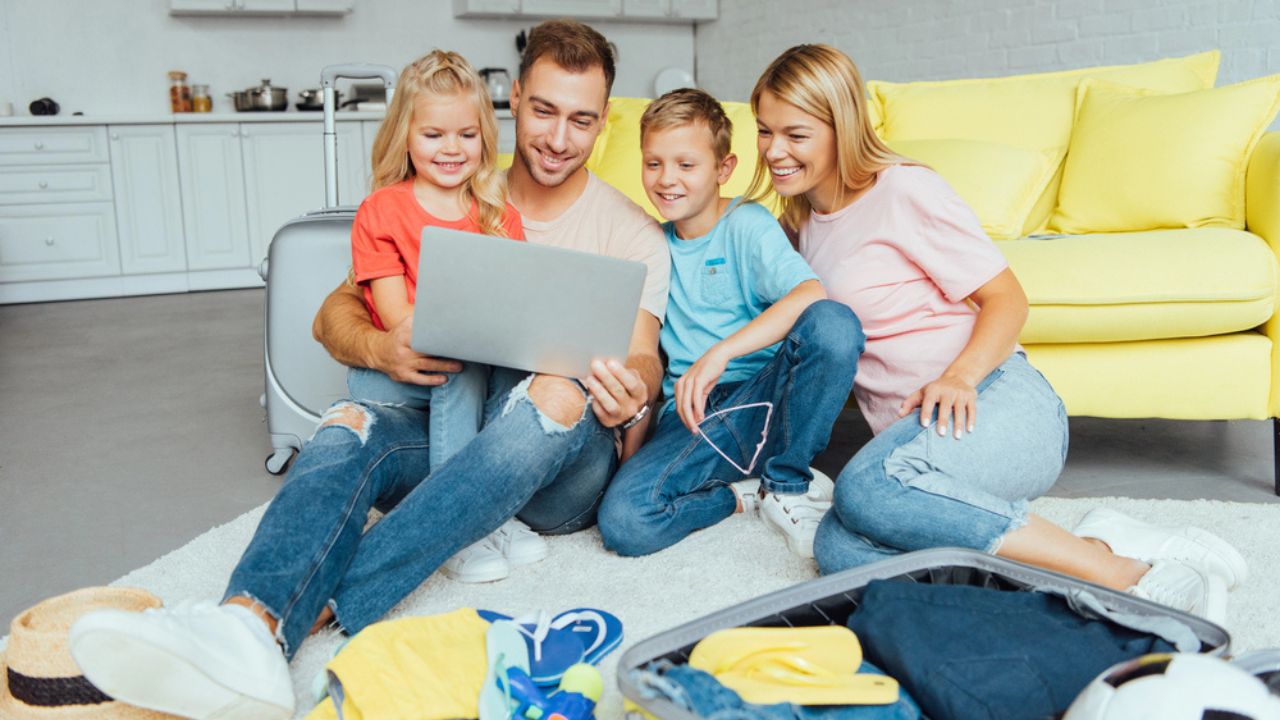 Happy family using laptop, planning summer vacation, packing luggage and having great time, travel concept